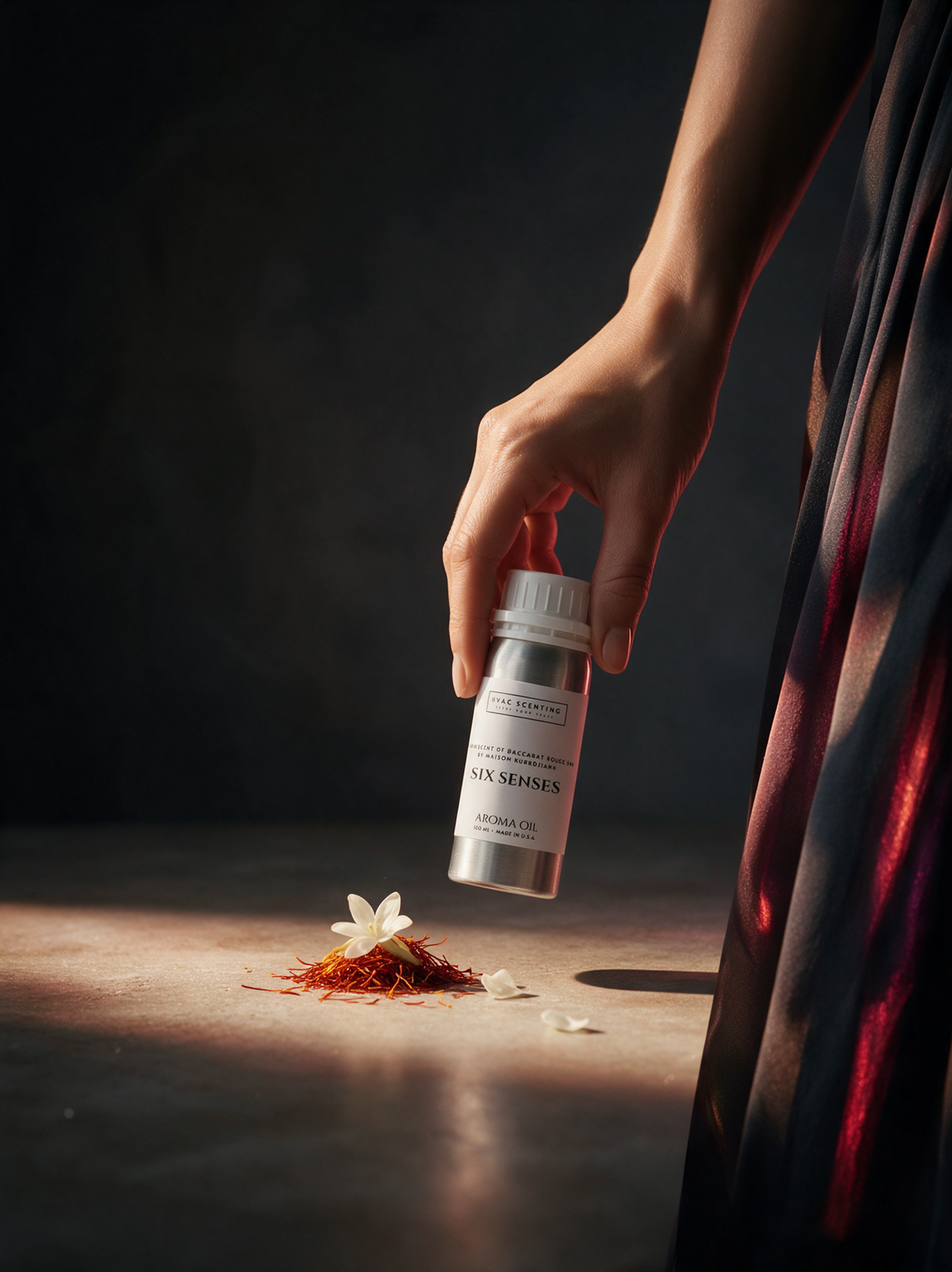 A hand holds a small silver bottle labeled 'SIX SENSES AROMA OIL' over a surface with a white flower and red spice pieces on a dark, moody background.